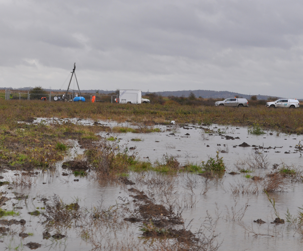 Lower Thames Crossing Ground Investigation Site Visit - View across a very wet and muddy field. Workers carrying out Ground Investigation work in the distance