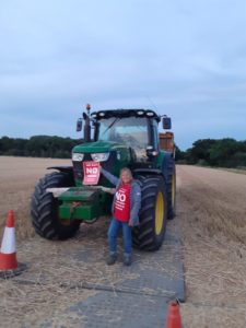 TCAG say NO to the LTC impacts on farming. Photo of TCAG VIce Chair, LEigh Hughes wearing a bright red 'No to LTC' campagin t-shirt, holding a 'No to LTC' poster in front of a local farmer's tractor